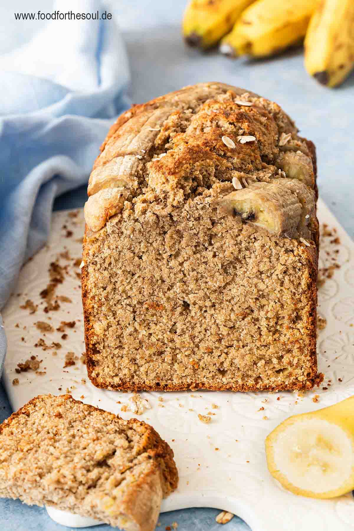 Bananenbrot mit Haferflocken serviert auf einem mit Backpapier belegten Frühstücksbrett