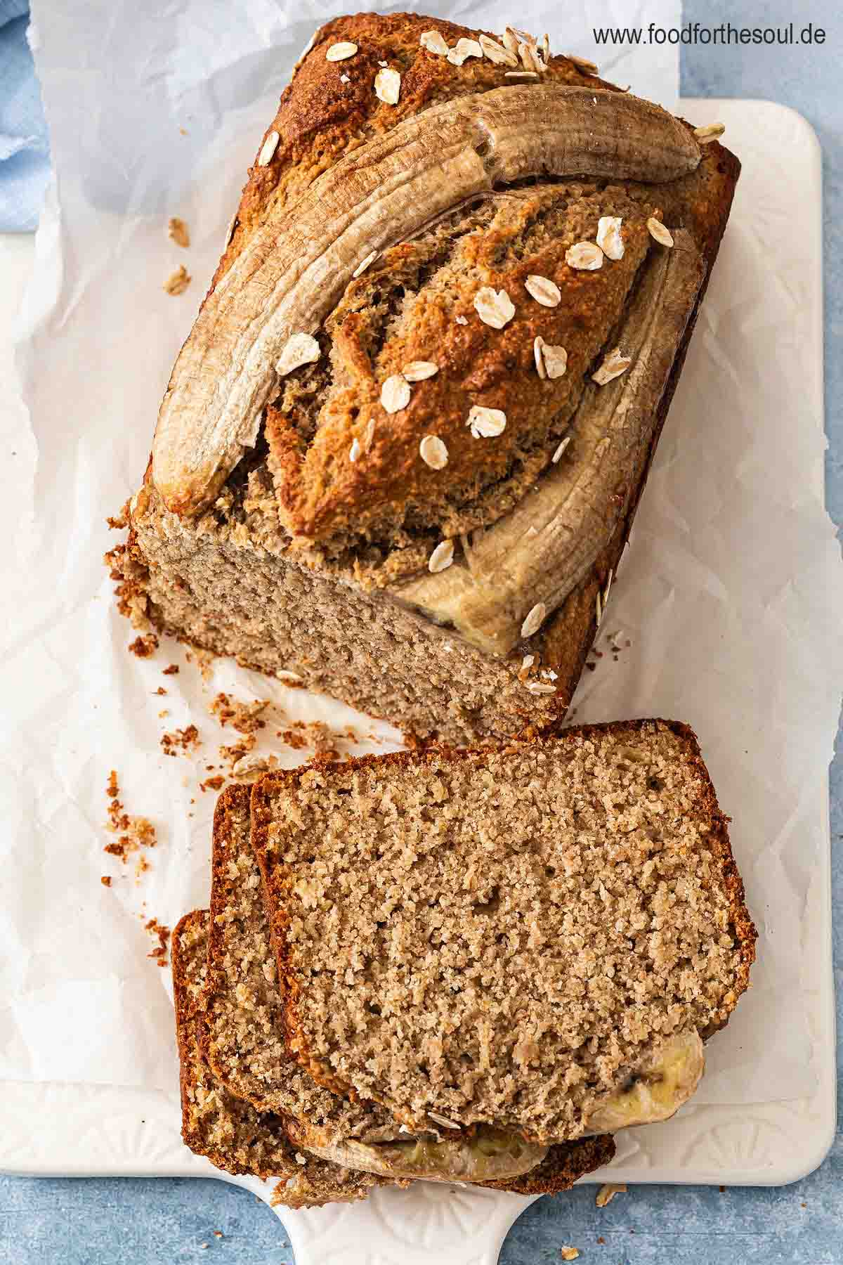 Bananenbrot mit Haferflocken serviert auf einem mit Backpapier belegten Frühstücksbrett
