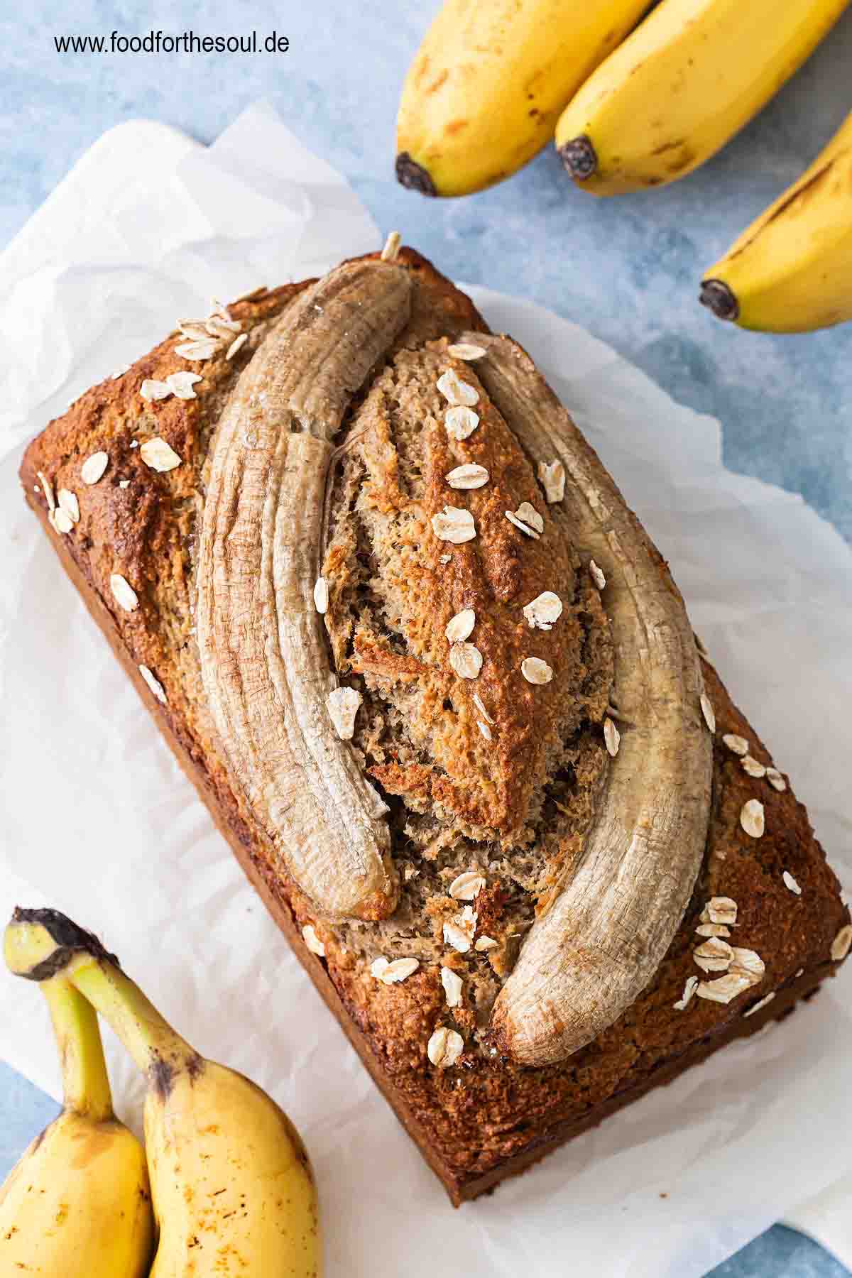 Bananenbrot mit Haferflocken dekoriert mit einer halbierten Banane und swrviert auf einem Frühstücksbrett