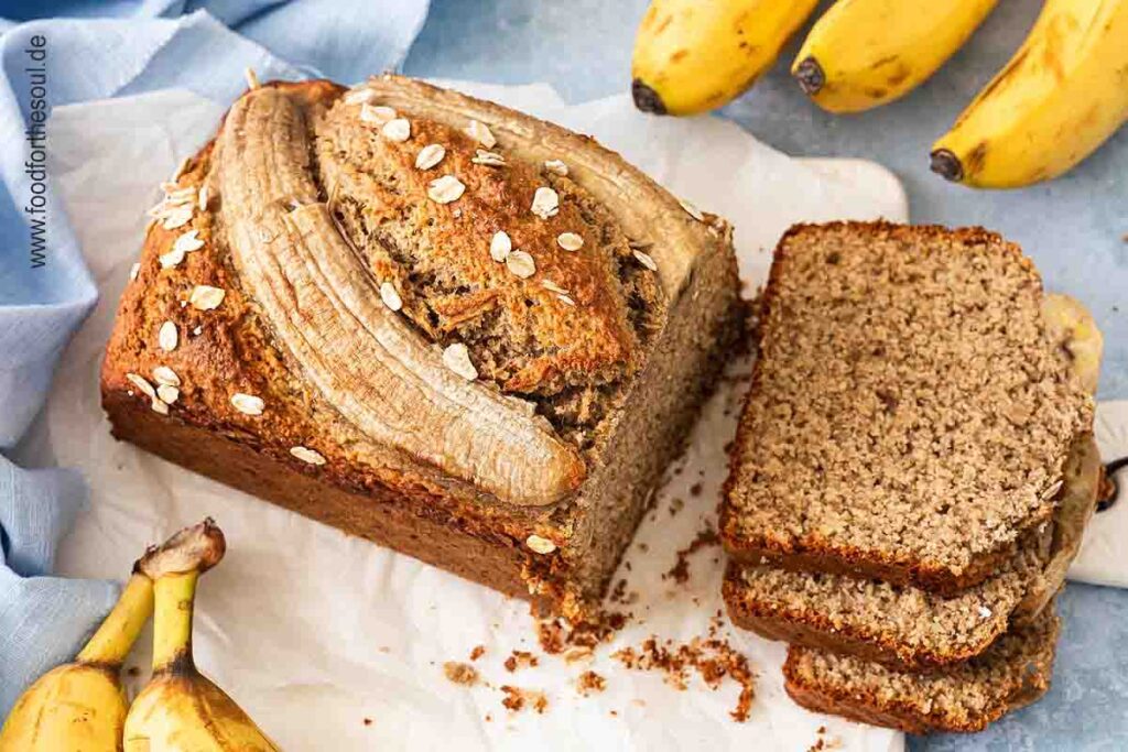 Bananenbrot mit Haferflocken serviert auf einem mit Backpapier belegten Frühstücksbrett