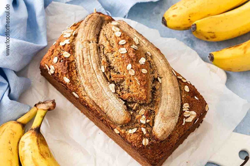 Bananenbrot mit Haferflocken dekoriert mit einer halbierten Banane und swrviert auf einem Frühstücksbrett