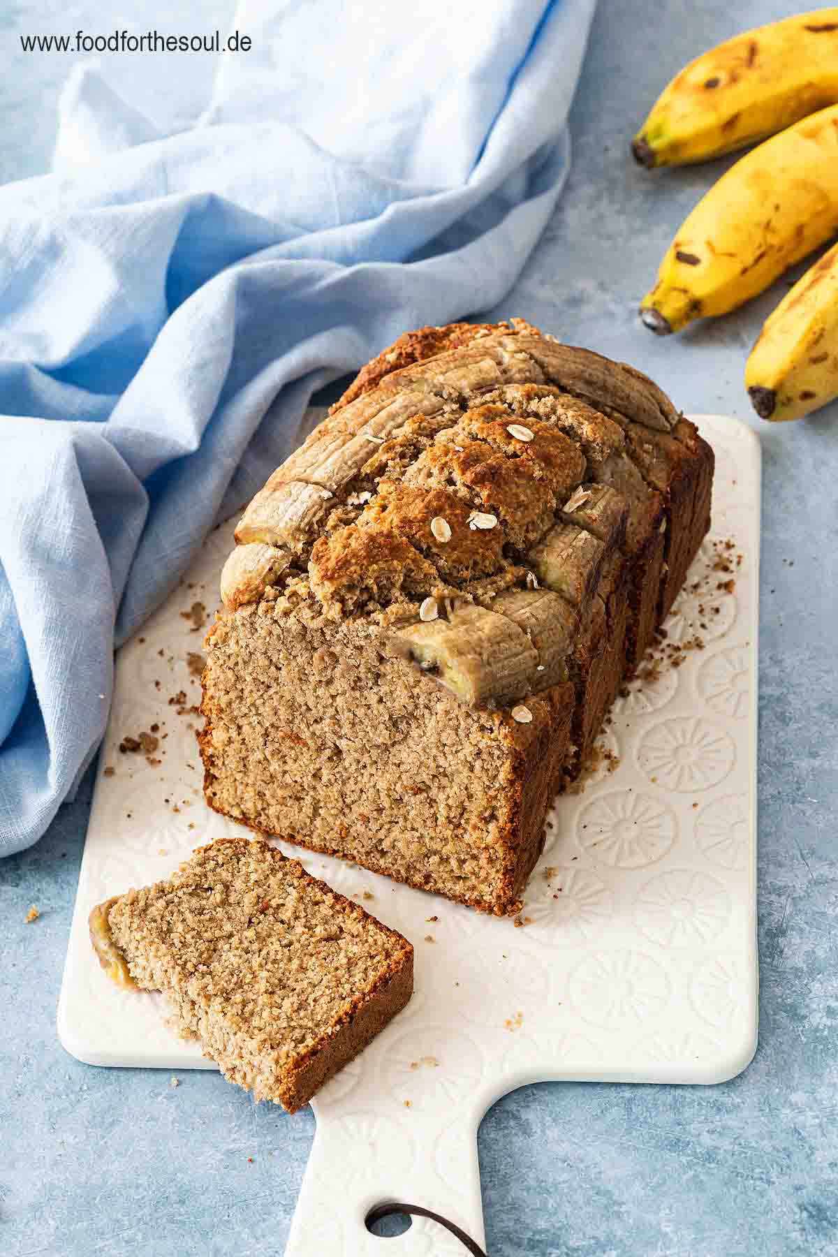 Bananenbrot mit Haferflocken serviert auf einem mit Backpapier belegten Frühstücksbrett