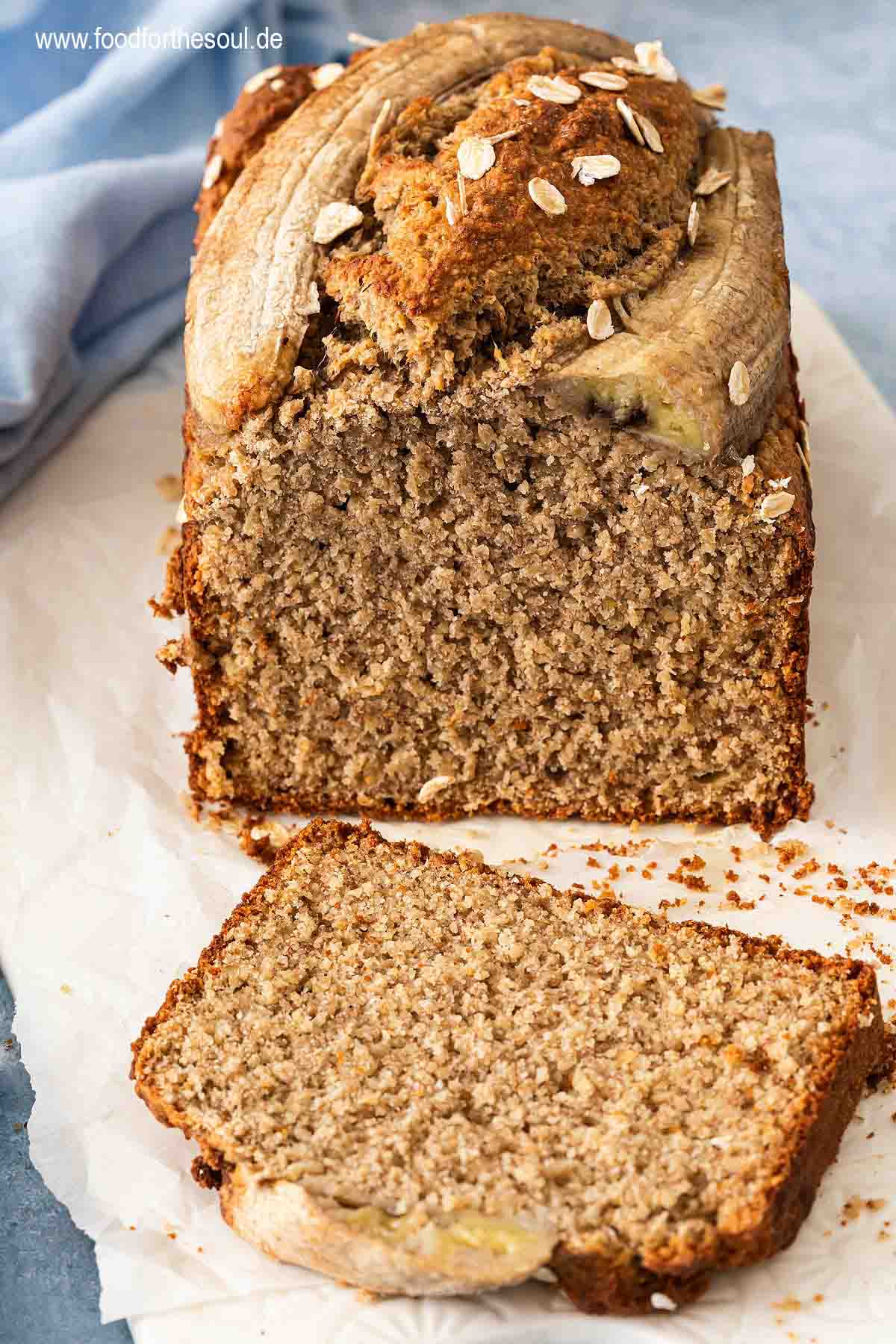 Bananenbrot mit Haferflocken serviert auf einem mit Backpapier belegten Frühstücksbrett
