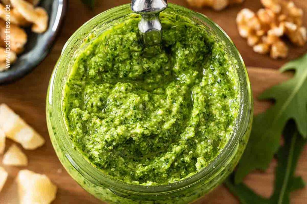 Selbstgemachtes Rucola Pesto in einem Glas umgeben von Zutaten