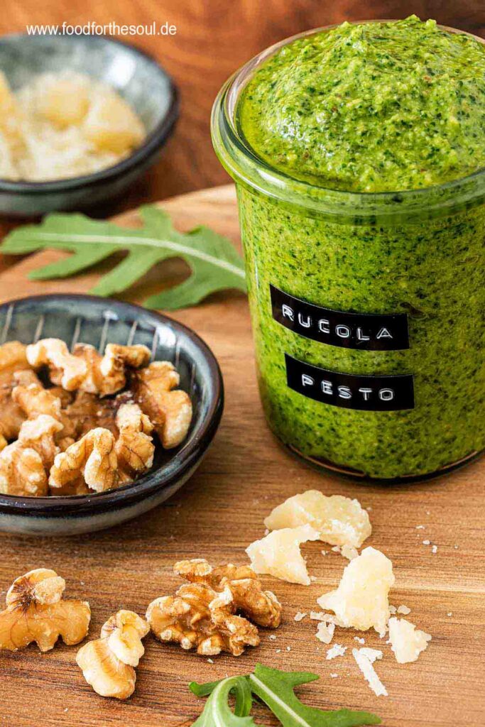 Selbstgemachtes Rucola Pesto in einem beschrifteten Glas umgeben von Zutaten