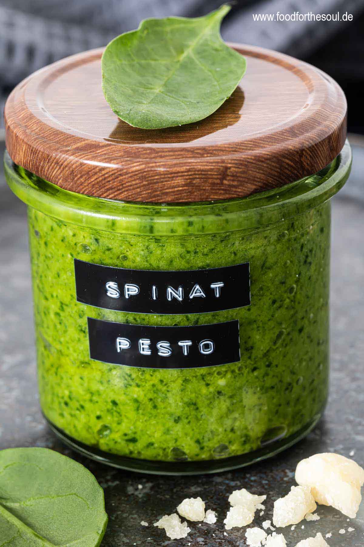 Frisch zubereitetes Spinat Pesto in einem Glas mit Deckel und Spinatblättern, daneben Parmesan