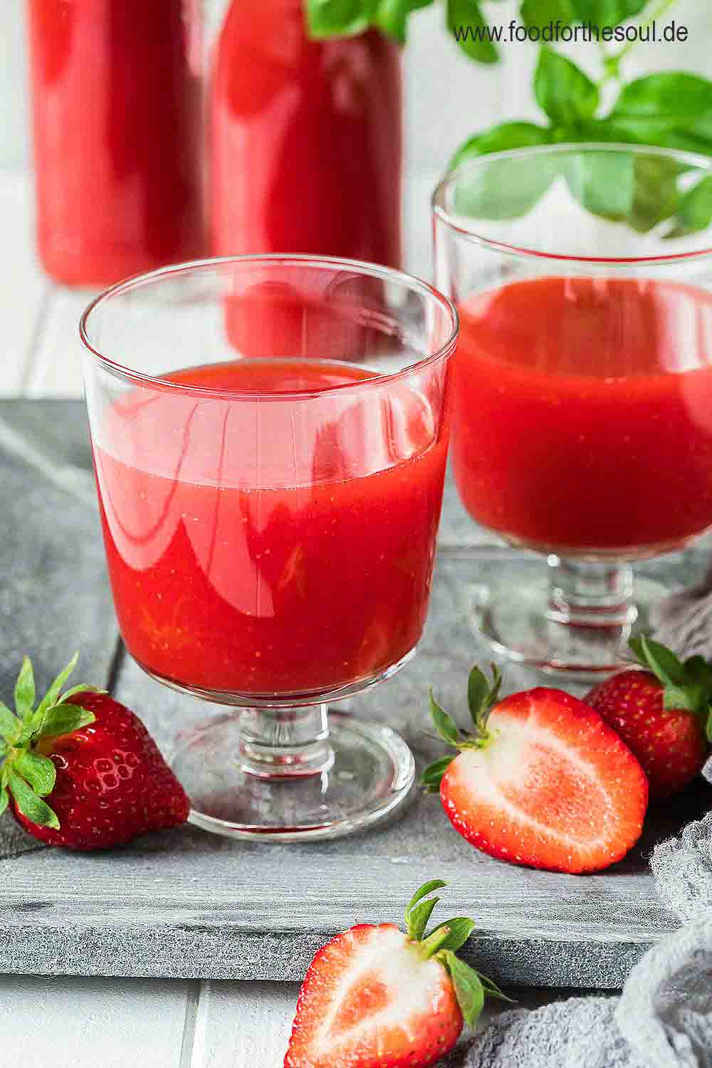 Selbstgemachter Erdbeer Limes in zwei Gläsern, daneben liegen Erdbeeren