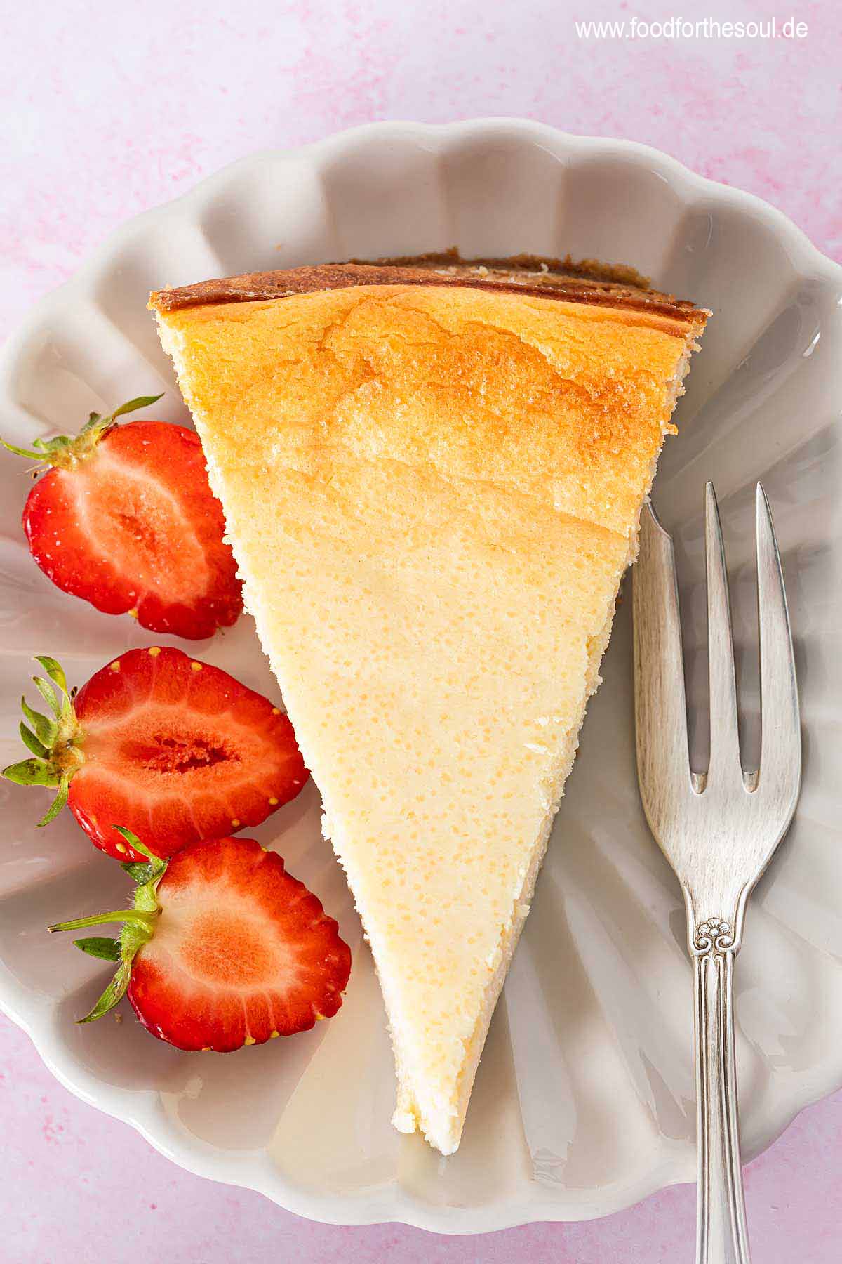 Ein Stück Quarkkuchen ohne Boden mit Grieß auf einem Teller mit Erdbeeren und Kuchengabel