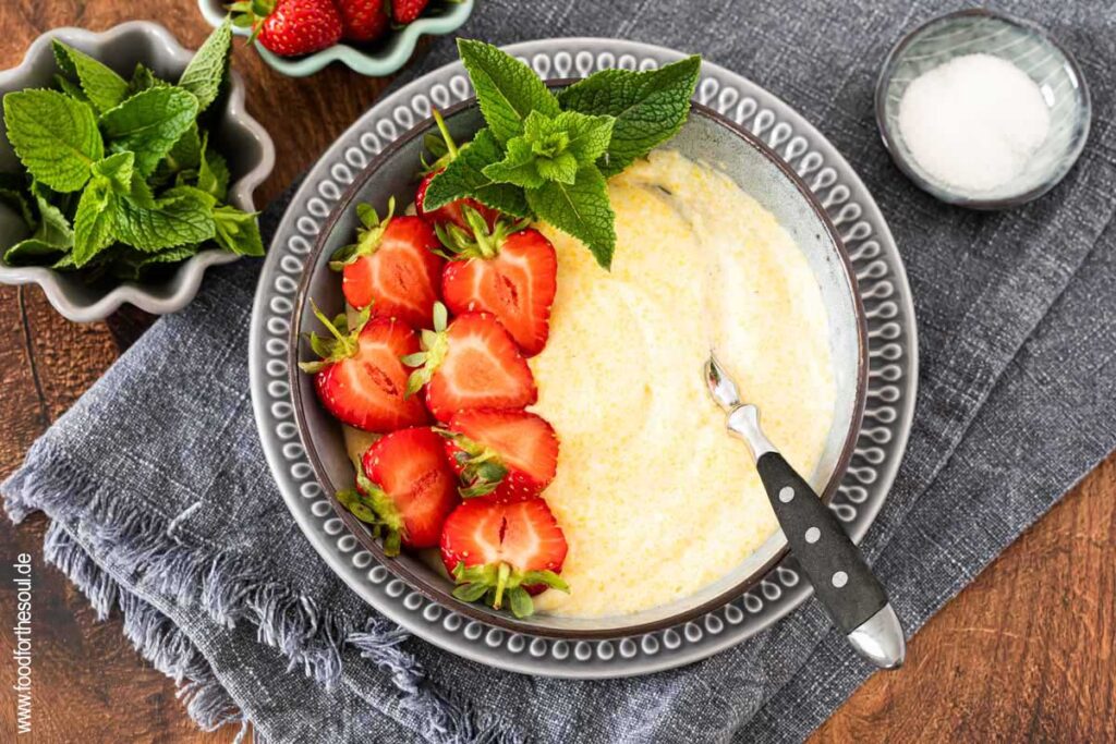 Süße Polenta - Maisbrei auf einem Teller garniert mit Erdbeeren und Minze