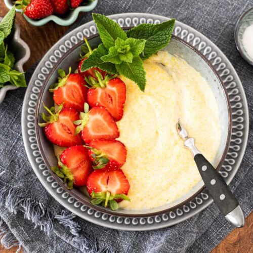 Süße Polenta - Maisbrei auf einem Teller garniert mit Erdbeeren und Minze