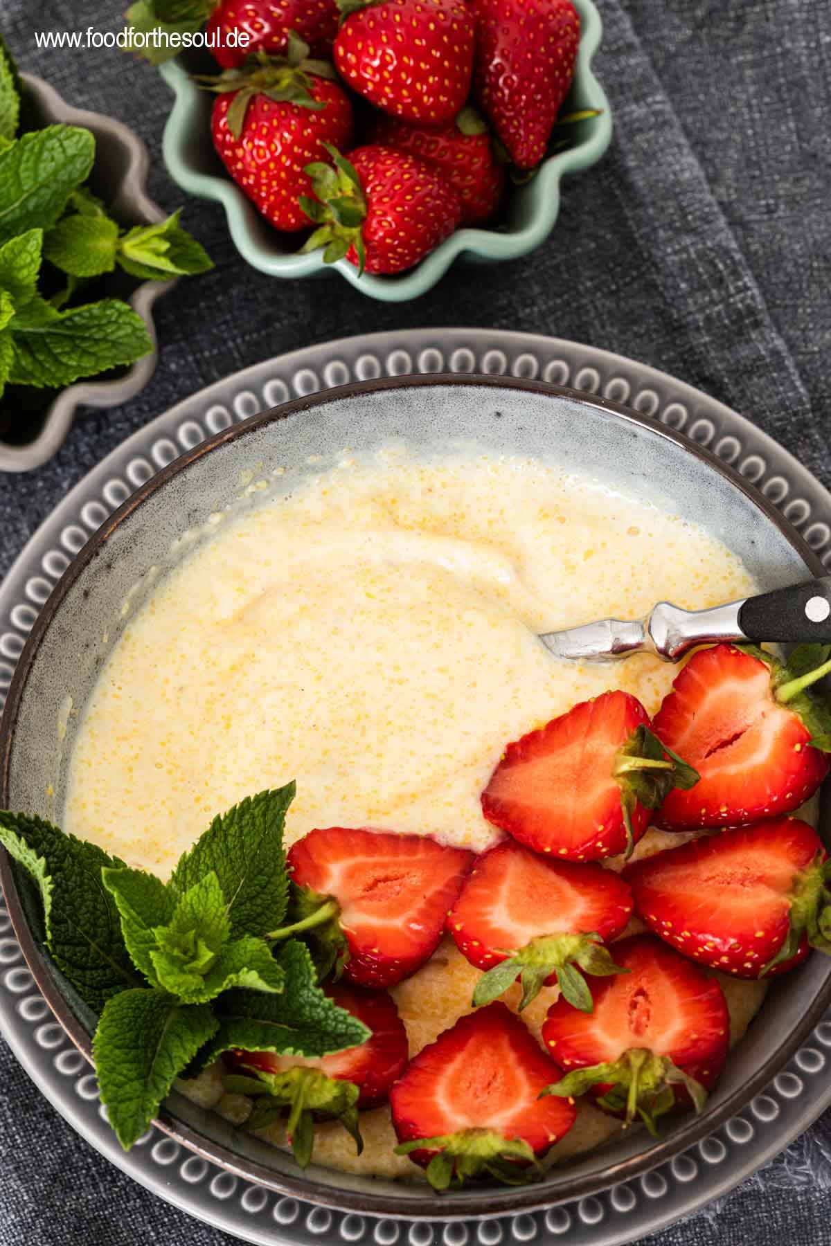 Süße Polenta - Maisbrei auf einem Teller garniert mit Erdbeeren und Minze
