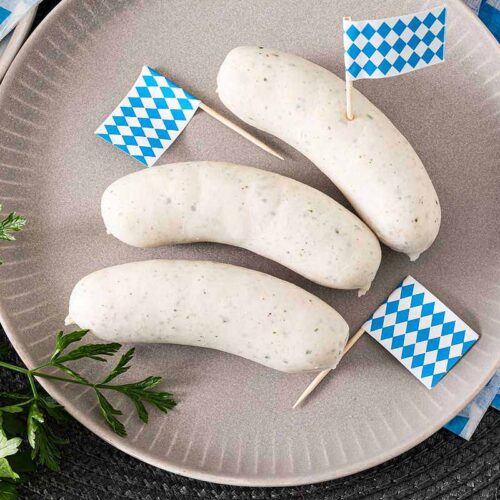 Bayerische Weißwurst serviert auf einem Teller und dekoriert mit Bayerischen Fähnchen