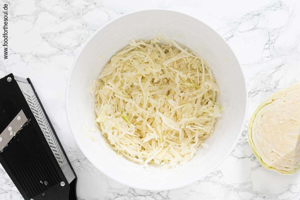 Weißkohl vierteln, Strunk entfernen und mit Gemüsehobel feine Streifen hobeln - Schritt 1