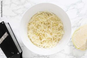 Weißkohl vierteln, Strunk entfernen und mit Gemüsehobel feine Streifen hobeln - Schritt 1