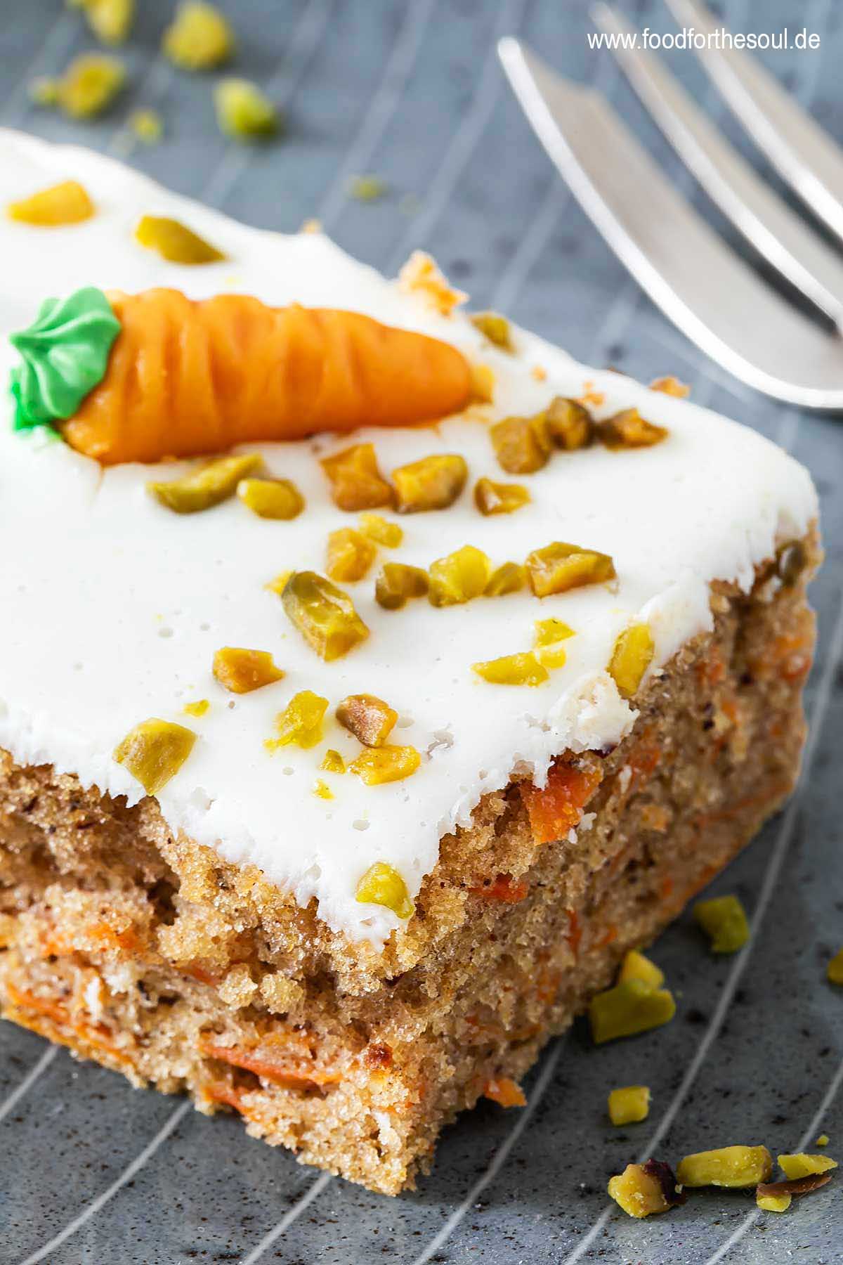 Ein Stück Karottenkuchen dekoriert mit Marzipan-Möhre und gehackten Pistazien