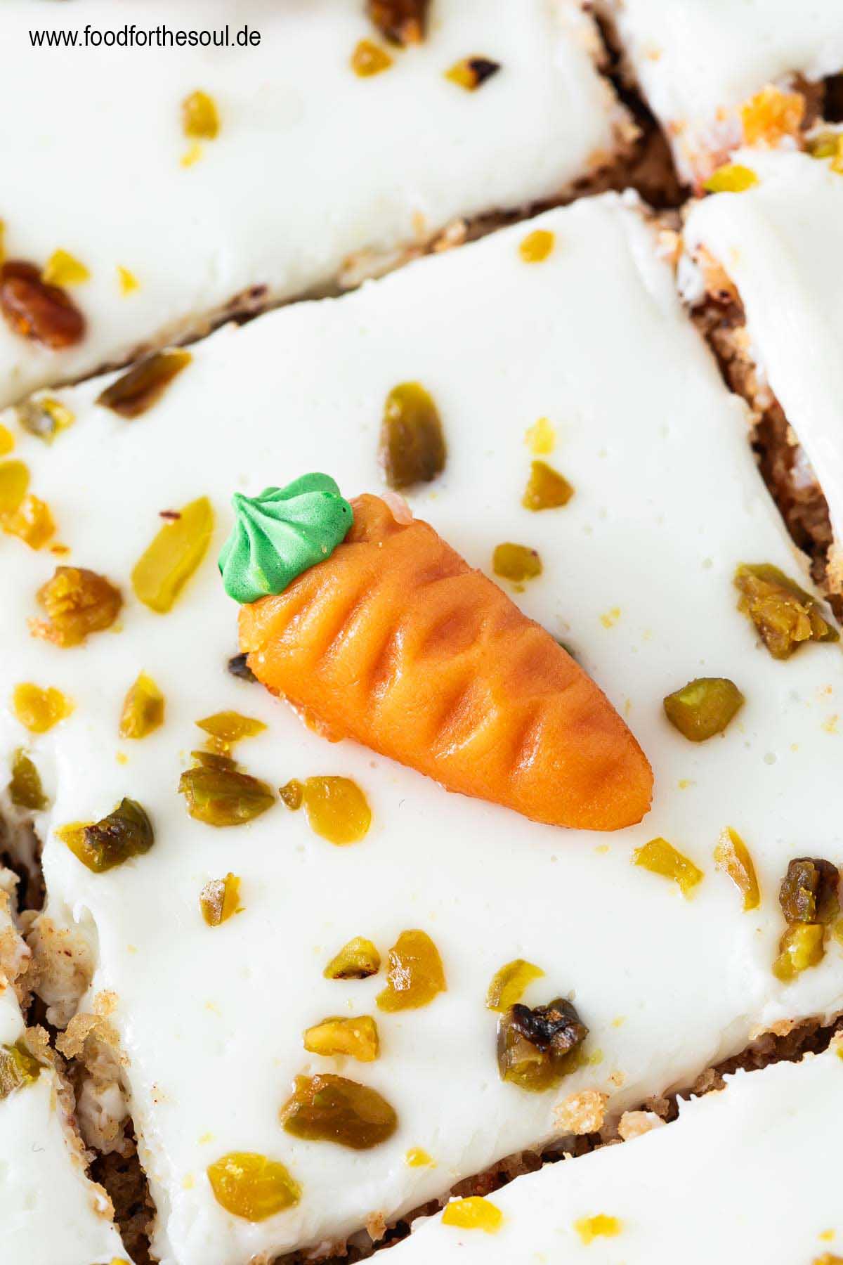 Ein Stück Karottenkuchen dekoriert mit Marzipan-Möhre und gehackten Pistazien