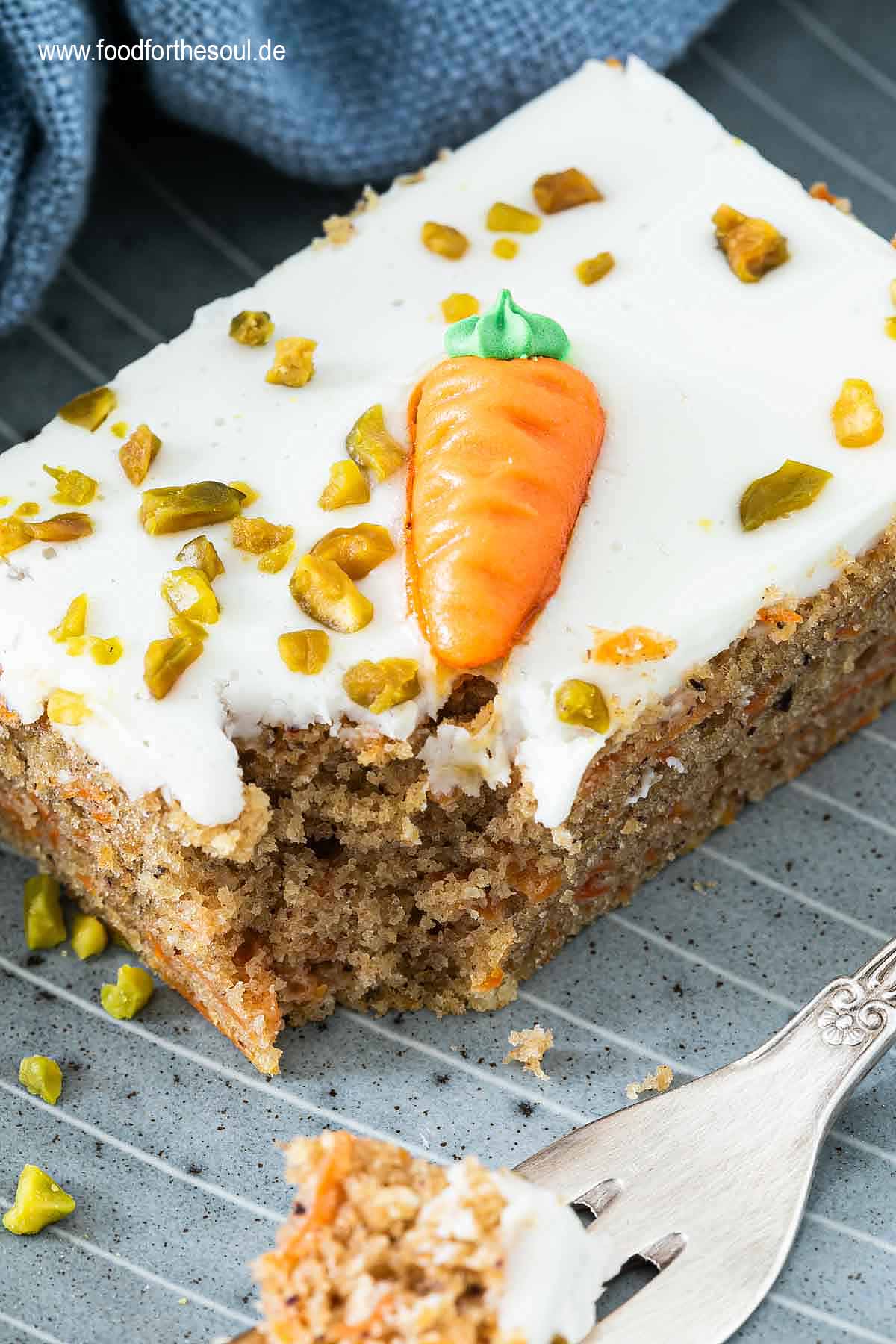 Ein Stück Karottenkuchen dekoriert mit Marzipan-Möhre und gehackten Pistazien