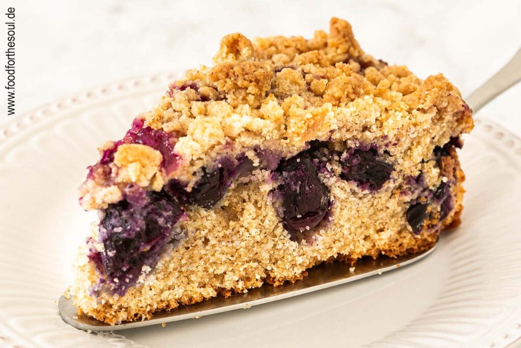 Ein Stück Traubenkuchen mit Streusel auf einem Teller mit Tortenheber