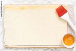 Blätterteig ausrollen und am Rand mit verquirltem Ei bepinseln - Schritt 2