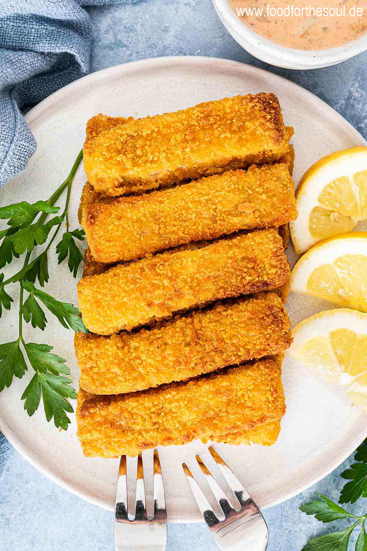 Knusprige Airfryer Fischstäbchen angerichtet mit Zitronenscheiben auf einem Teller