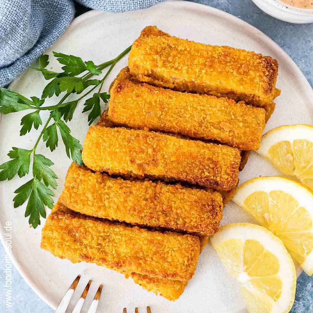 Knusprige Airfryer Fischstäbchen angerichtet mit Zitronenscheiben auf einem Teller