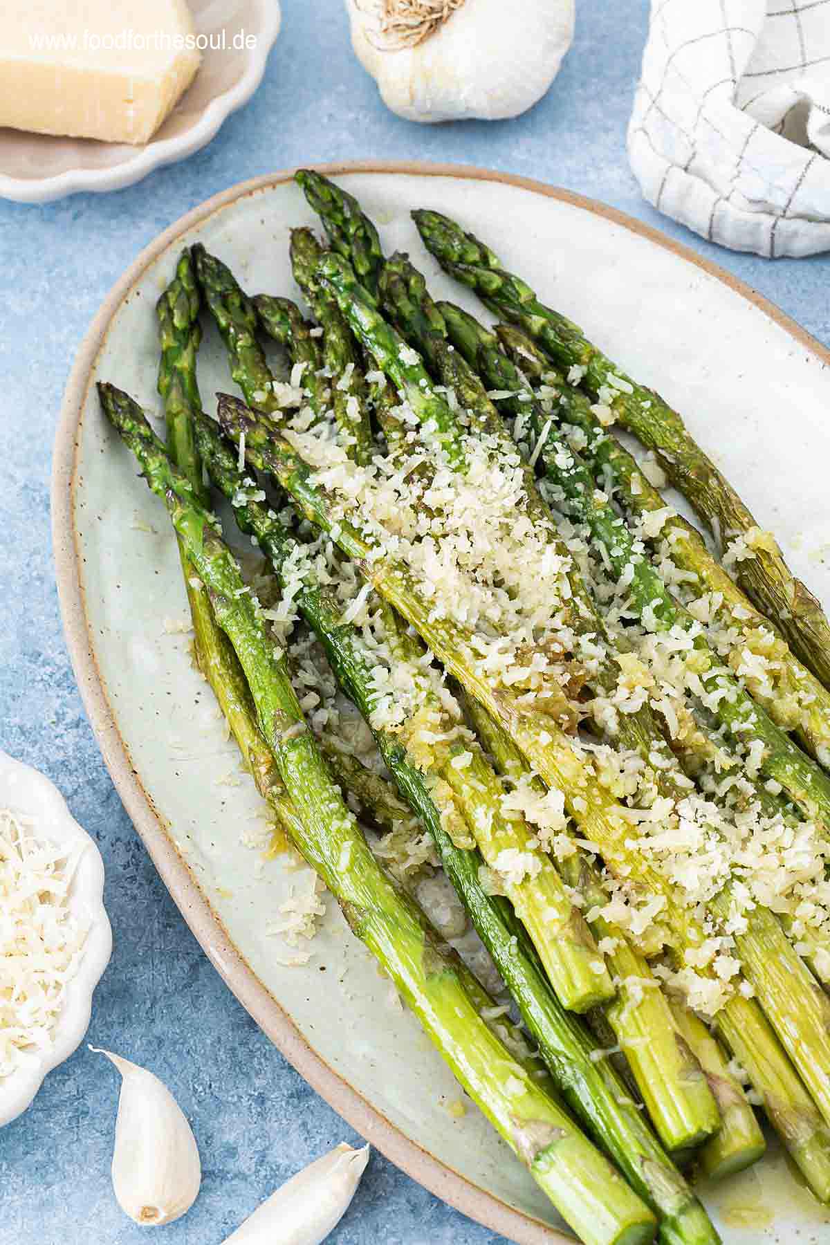 Grüner Spargel angerichtet mit Parmesan und Knoblauch auf einer Servierplatte