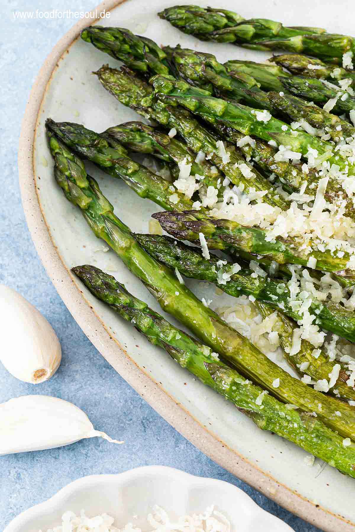 Grüner Spargel angerichtet mit Parmesan und Knoblauch auf einer Servierplatte