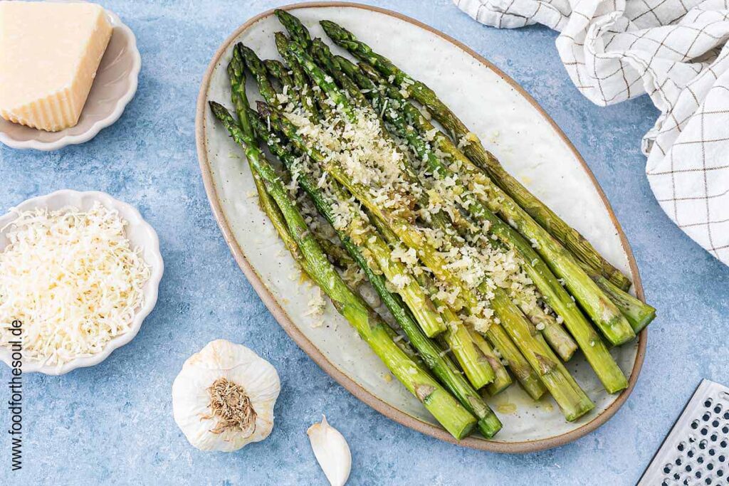 Grüner Spargel angerichtet mit Parmesan und Knoblauch auf einer Servierplatte