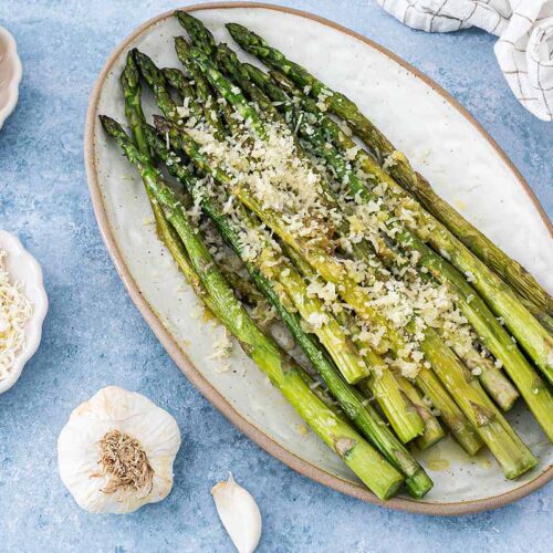 Grüner Spargel angerichtet mit Parmesan und Knoblauch auf einer Servierplatte