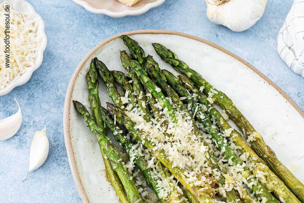 Grüner Spargel angerichtet mit Parmesan und Knoblauch auf einer Servierplatte