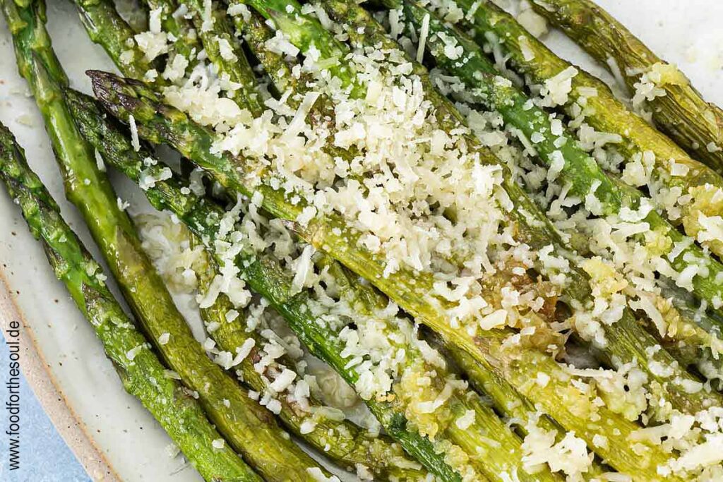 Grüner Spargel angerichtet mit Parmesan und Knoblauch auf einer Servierplatte