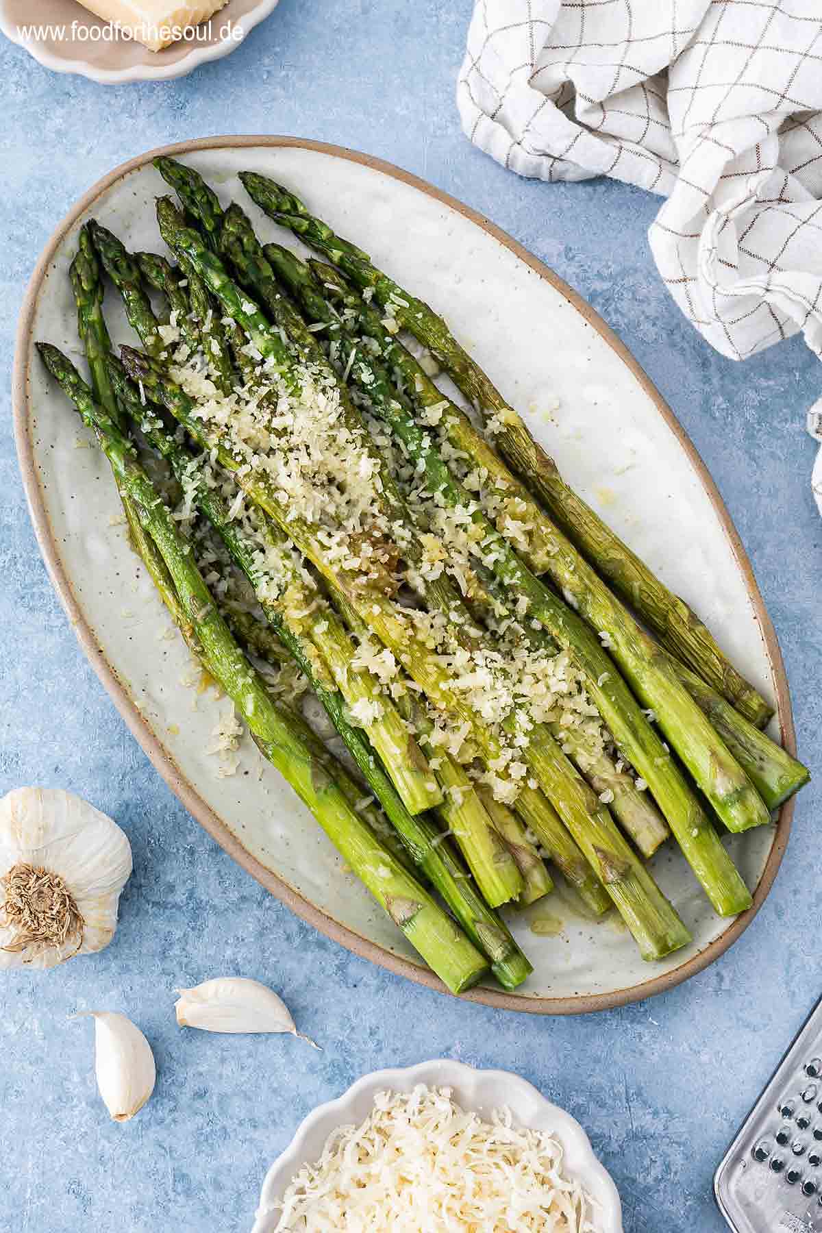 Grüner Spargel angerichtet mit Parmesan und Knoblauch auf einer Servierplatte