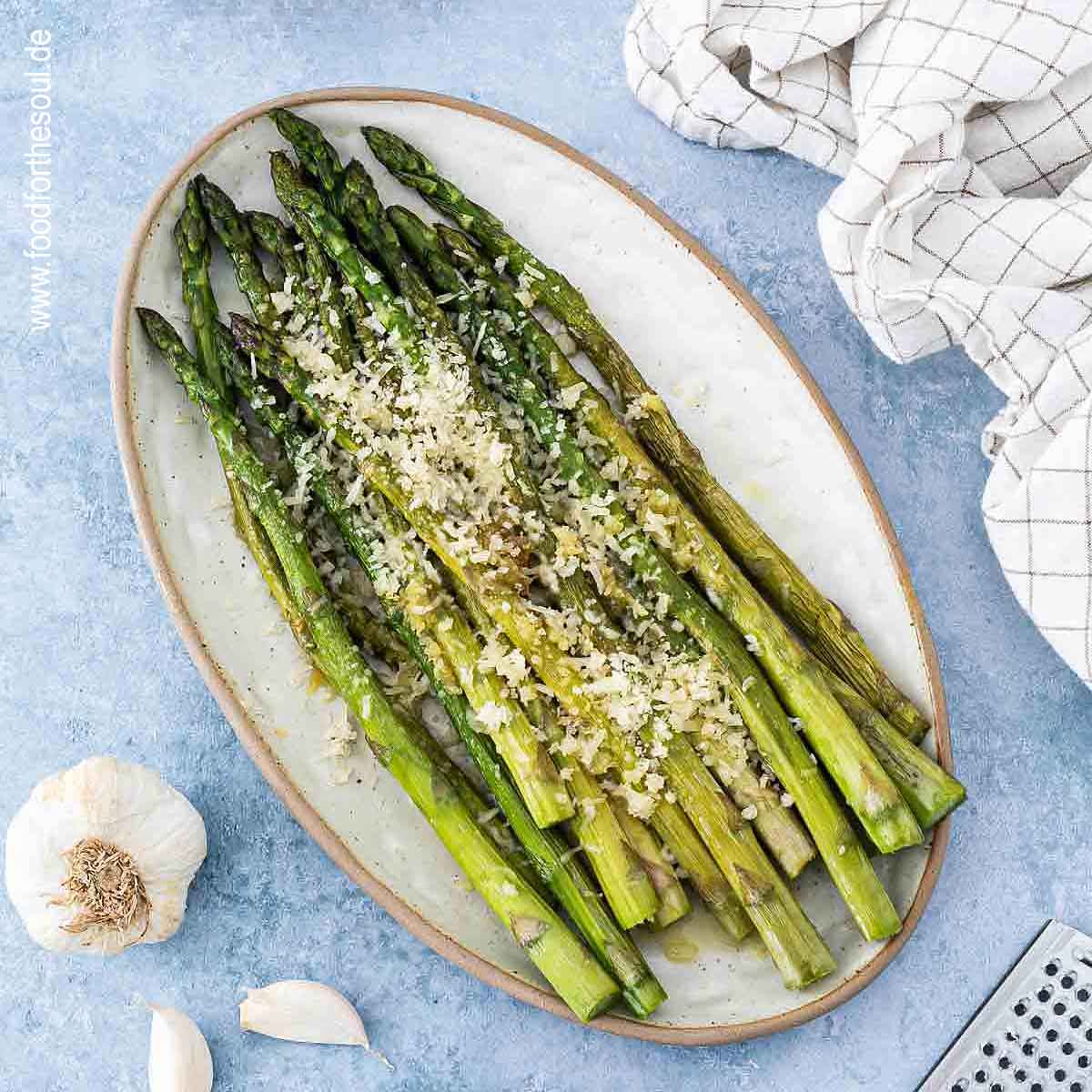 Grüner Spargel angerichtet mit Parmesan und Knoblauch auf einer Servierplatte