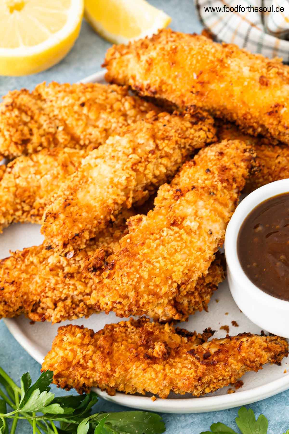 Panierte Hähncheninnenfilets angerichtet auf einem Teller mit BBQ Sauce