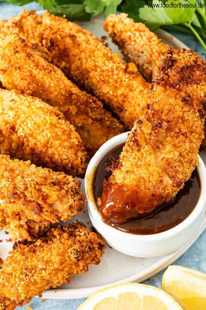 Panierte Hähncheninnenfilets angerichtet auf einem Teller mit BBQ Sauce