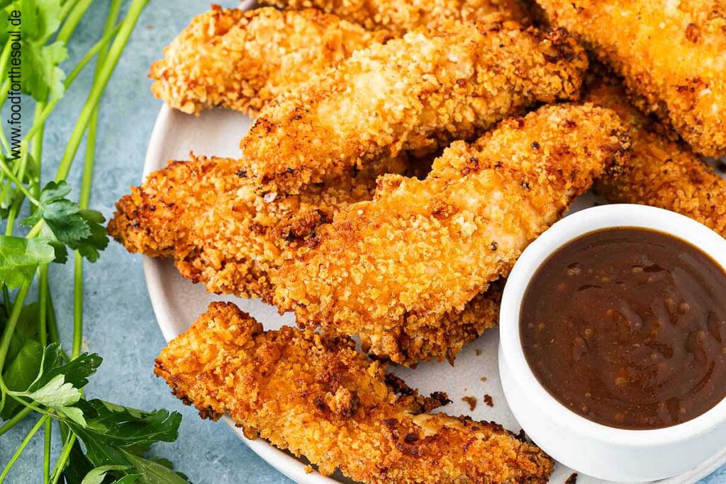 Panierte Hähncheninnenfilets angerichtet auf einem Teller mit BBQ Sauce