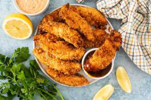 Panierte Hähncheninnenfilets angerichtet auf einem Teller mit BBQ Sauce