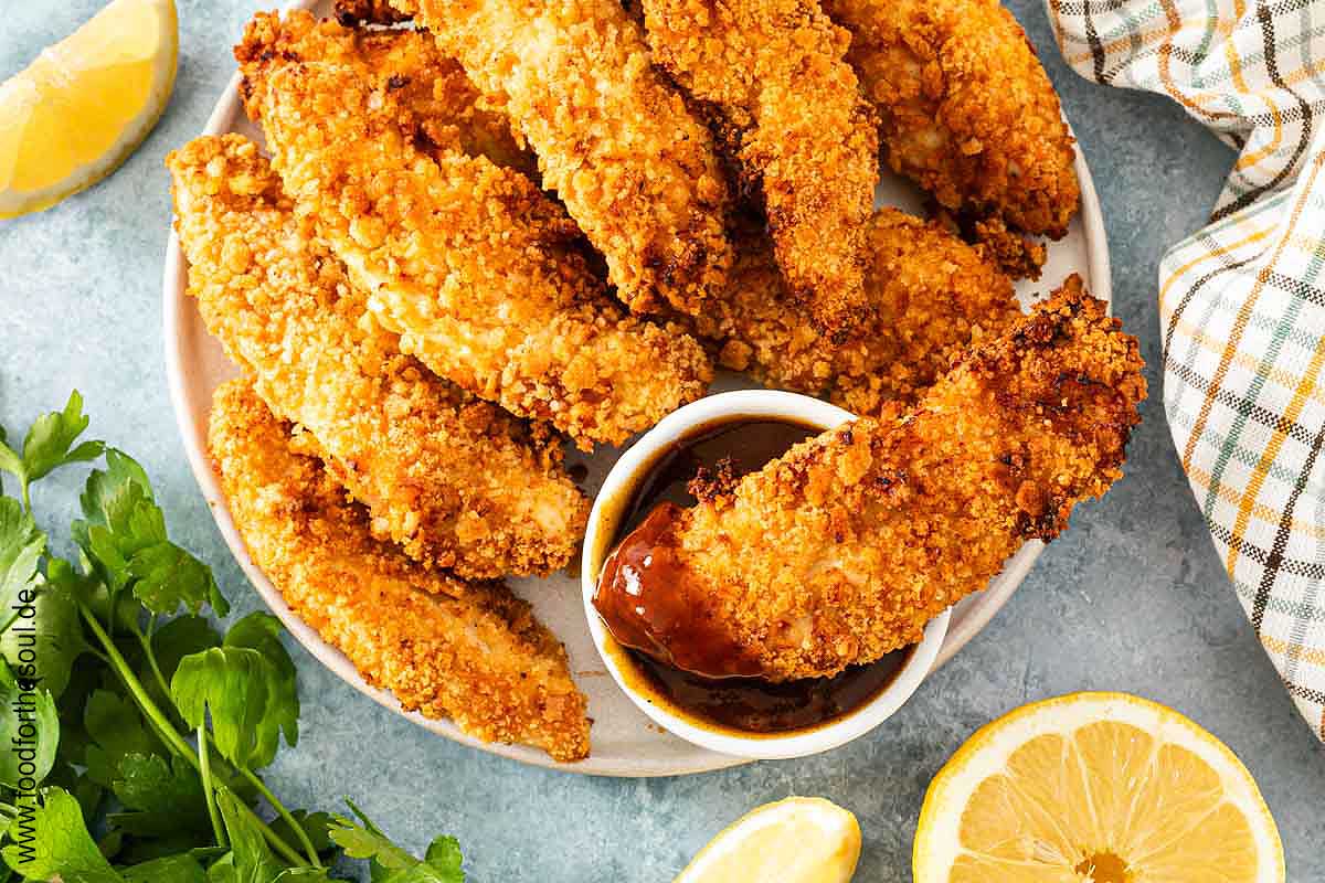 Panierte Hähncheninnenfilets angerichtet auf einem Teller mit BBQ Sauce