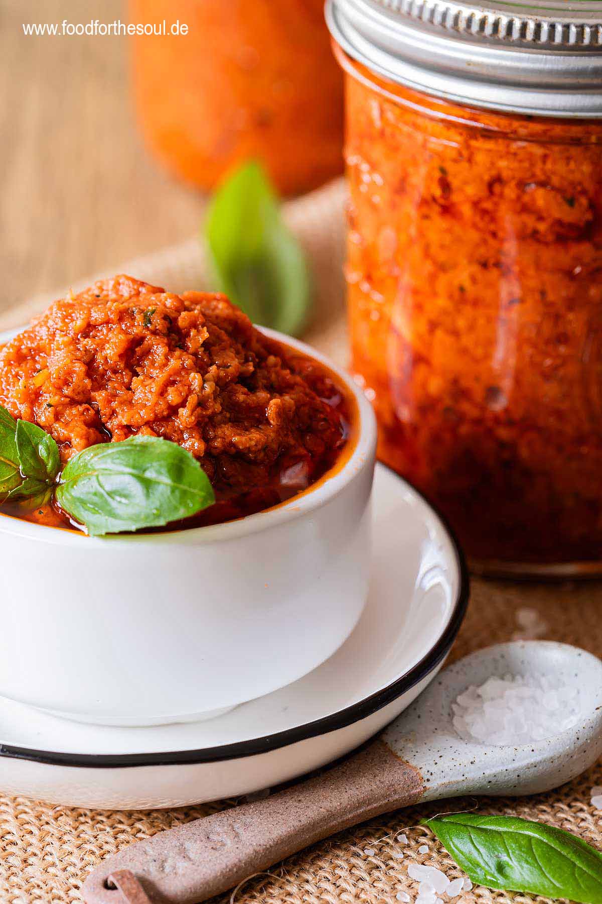 Selbstgemachtes Tomatenpesto in einer Schale und Gläsern, garniert mit Basilikum