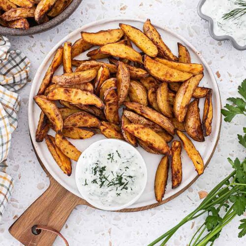 Knusprige Kartoffelspalten auf einem Teller angerichtet mit Tzatziki