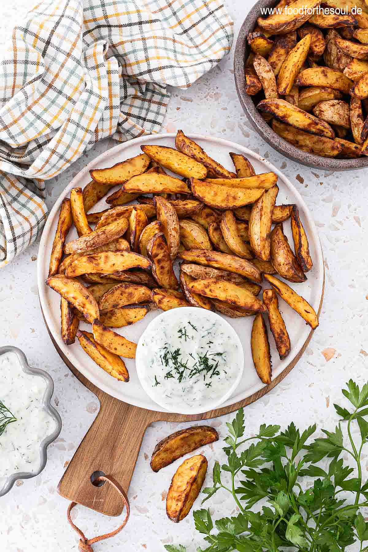 Knusprige Kartoffelspalten auf einem Teller angerichtet mit Tzatziki