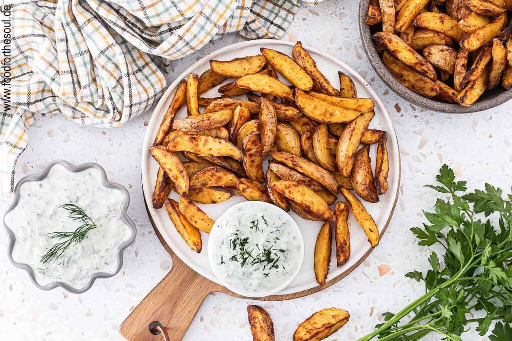 Knusprige Kartoffelspalten auf einem Teller angerichtet mit Tzatziki