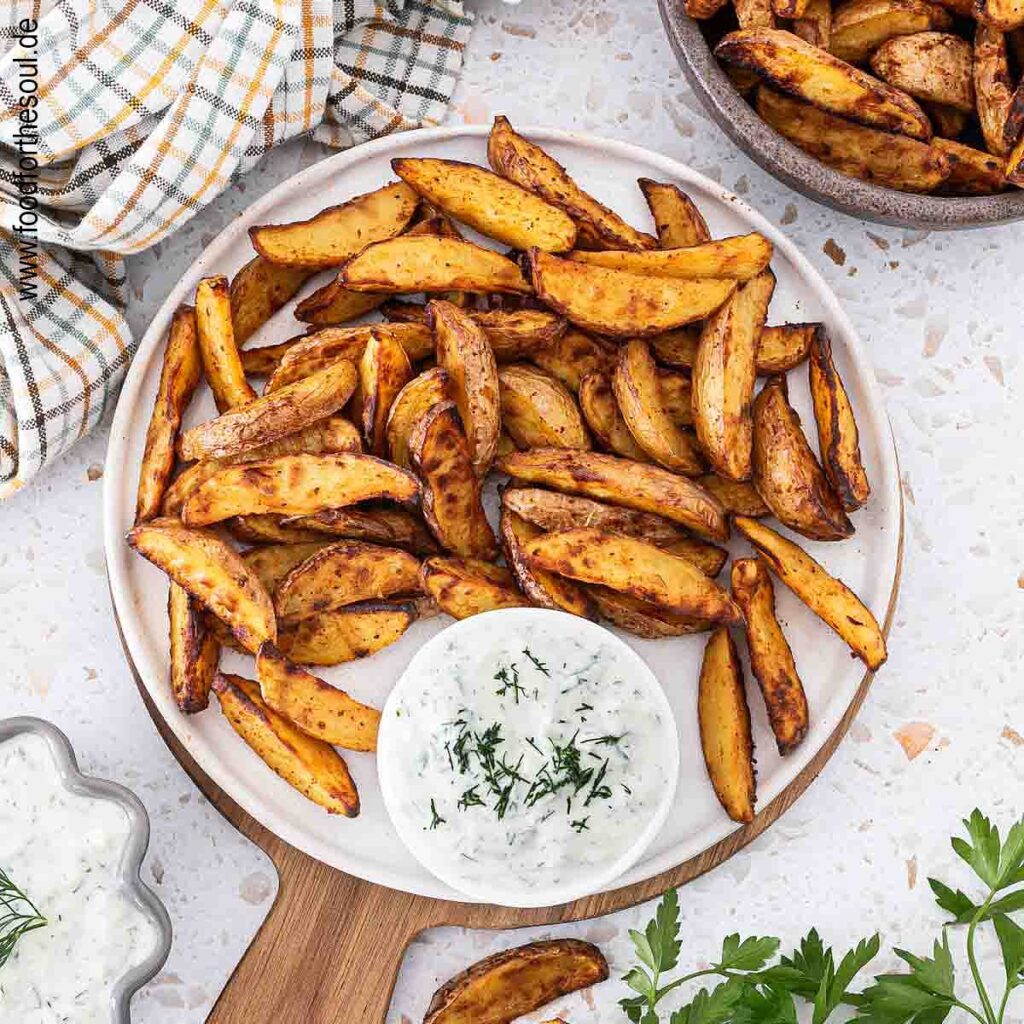 Knusprige Kartoffelspalten auf einem Teller angerichtet mit Tzatziki