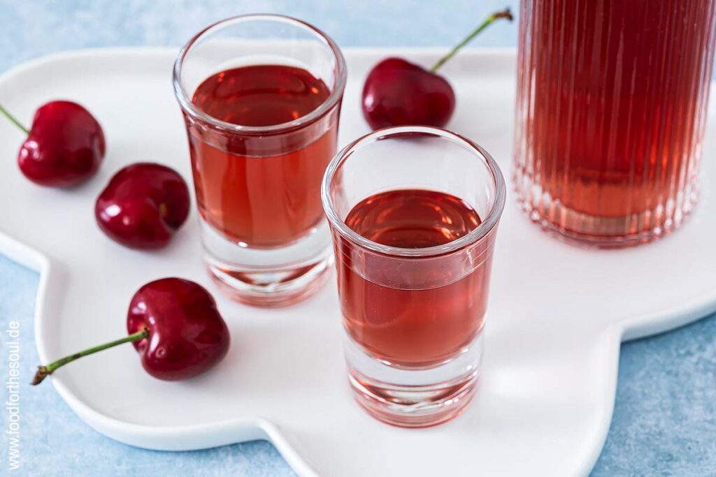 Selbstgemachter Kirschlikör in einer Flasche und zwei Schnapsgläsern
