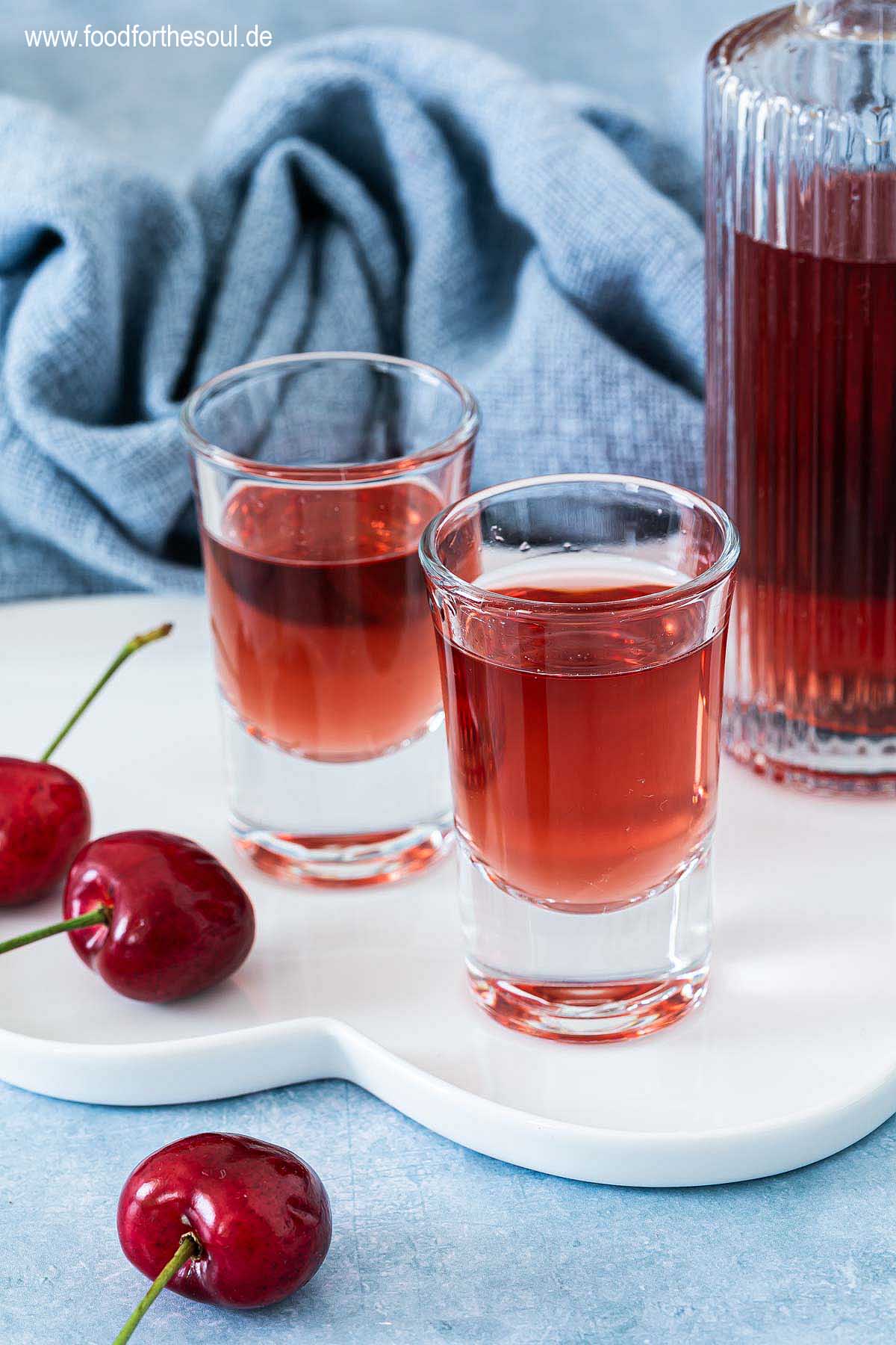 Selbstgemachter Kirschlikör in einer Flasche und zwei Schnapsgläsern