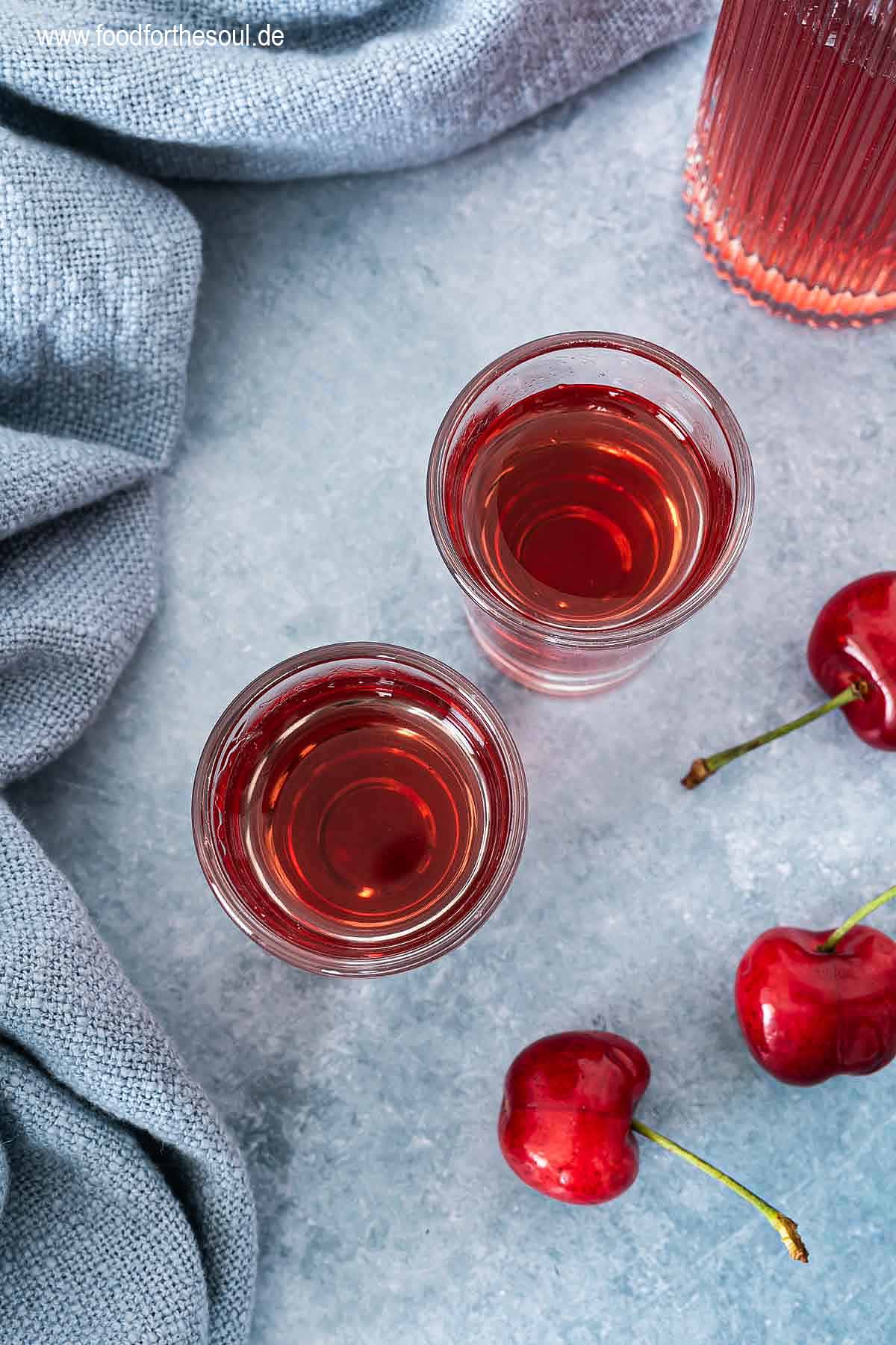 Selbstgemachter Kirschlikör in einer Flasche und zwei Schnapsgläsern