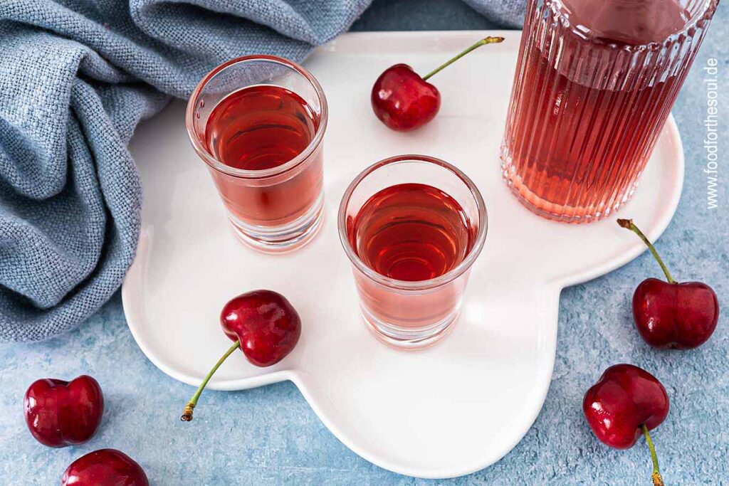 Selbstgemachter Kirschlikör in einer Flasche und zwei Schnapsgläsern