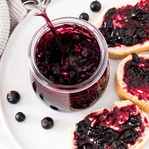 Selbstgemachte Johannisbeermarmelade in einem Glas und auf Baguettescheiben
