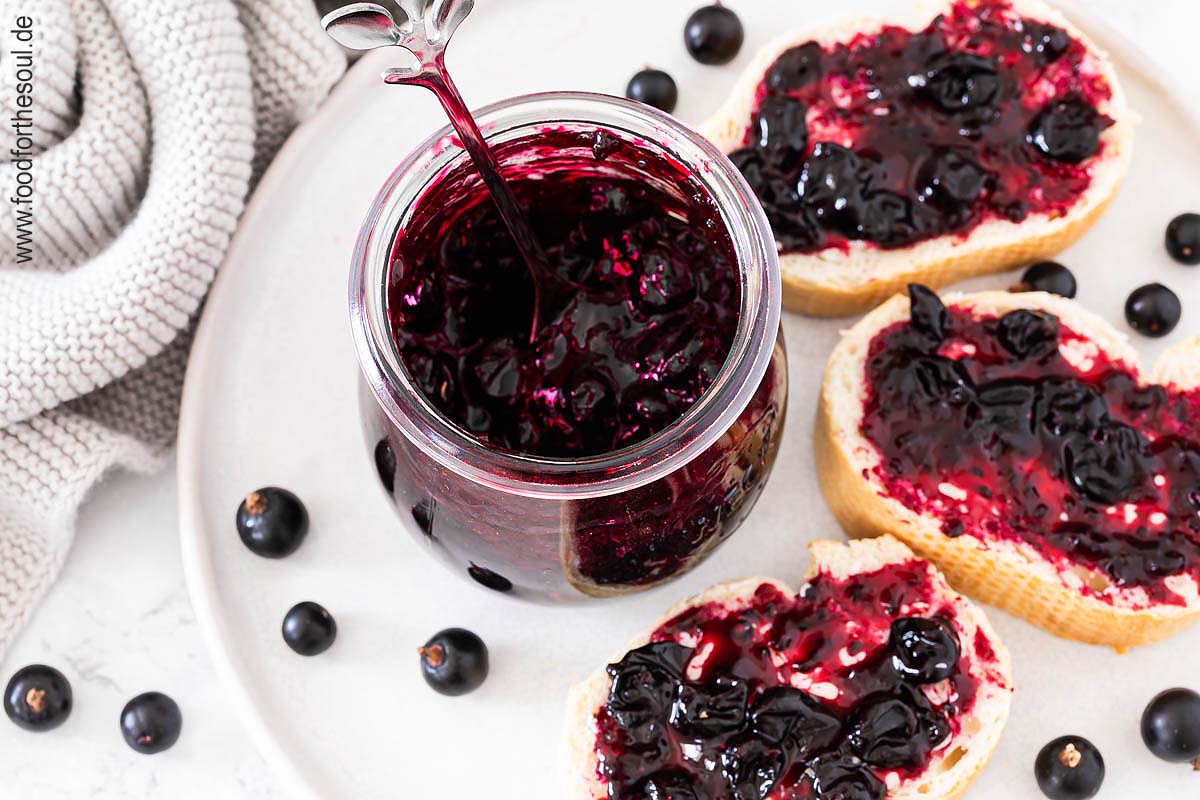 Selbstgemachte Johannisbeermarmelade in einem Glas und auf Baguettescheiben