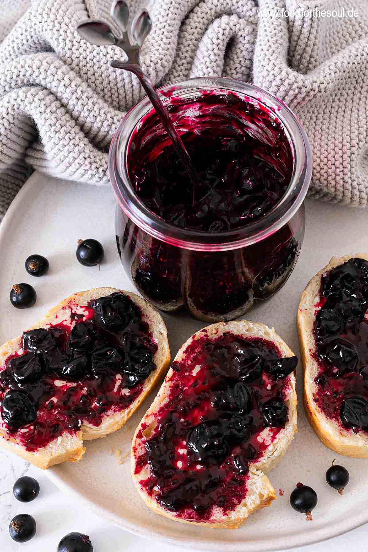 Selbstgemachte Johannisbeermarmelade in einem Glas und auf Baguettescheiben